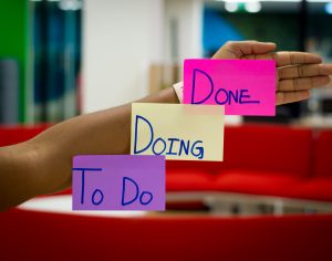 Hand with "To Do," "Doing," and "Done" stickers