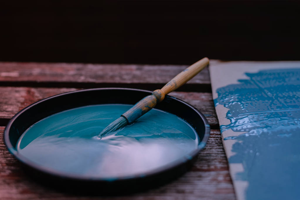 A paintbrush rests in a bowl of blue paint