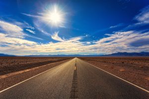 Desert road stretches to distant horizon under a harsh sun