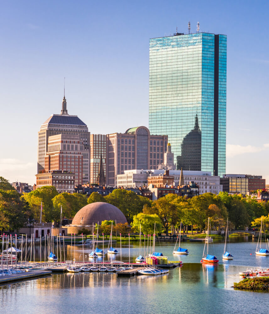 Boston skyline at dusk, with boats bobbing on the calm harbor